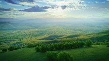Aerial Backward Motion View On Beautiful Valley Landscape, Horizon Green Grass Meadows, Mountain Slopes And Shining Sun Rays, Yellow Blue Cloudy Sky, Sunny Day