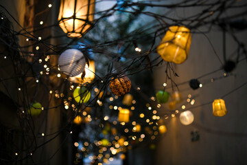 Colorful lampions and lanterns up a tree at night in the garden. A wedding, event or festival banquet decoration at night. Garlands of lamps on a tree branches. Row of paper lampions.