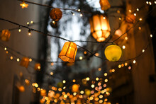 Colorful Lampions And Lanterns Up A Tree At Night In The Garden. A Wedding, Event Or Festival Banquet Decoration At Night. Garlands Of Lamps On A Tree Branches. Row Of Paper Lampions.