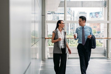 Two colleagues walking and talking in office hall.
Coworkers walking with coffee in modern office building