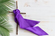 cross with purple sash on white wood background with palms