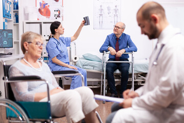 Nurse looking at radiography of handicapped patient sitting on wheelchair. Man with disabilities ,walking frame sitting in hospital bed. Health care system, clinic patients.