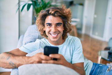 Wall Mural - Young hispanic man smiling happy using smartphone at home