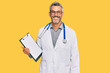 Middle age grey-haired man wearing doctor stethoscope holding clipboard looking positive and happy standing and smiling with a confident smile showing teeth