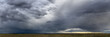 canvas print picture - Dramatic blue-gray storm clouds over a very wide panoramic prairie landscape with a gravel road extending off into the distance.
