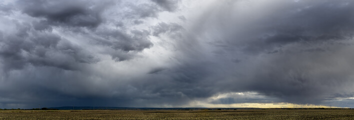 Dramatic blue-gray storm clouds over a very wide panoramic prairie landscape with a gravel road extending off into the distance.
