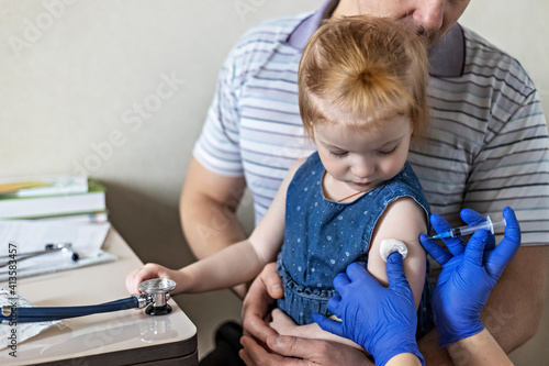 A little girl with her father in the doctor\'s office at the clinic is being vaccinated against the coronavirus.The concept of vaccination, immunization, prevention against Covid-19.