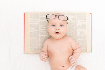 Wall Mural - baby with glasses and a book on a light background, learning and development concept