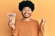 © Krakenimages.com - Young african american man with afro hair holding 5000 hungarian forint banknotes screaming proud, celebrating victory and success very excited with raised arm