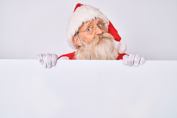 Wall Mural - Old senior man with grey hair and long beard wearing santa claus costume holding banner smiling looking to the side and staring away thinking.