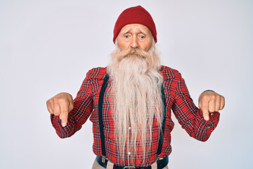 Wall Mural - Old senior man with grey hair and long beard wearing hipster look with wool cap pointing down looking sad and upset, indicating direction with fingers, unhappy and depressed.