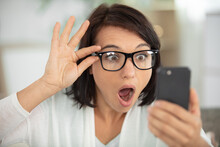 Woman Wearing Eyeglasses Looking With Shock At Smartphone
