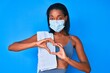 canvas print picture - Young african american woman wearing sportswear and medical mask smiling in love showing heart symbol and shape with hands. romantic concept.