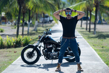 Male With A Black Shirt Holding His Arms Behind His Head And His Motorbike In The Background