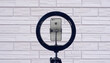 © MaskaRad - ring lamp and a smartphone on a tripod against the background of a light brick wall.