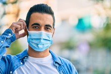 Young Hispanic Man Putting On Medical Mask Standing At The City.