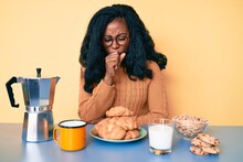 Beautiful African Woman Sitting On The Table Eating Breakfast In The Morning Feeling Unwell And Coughing As Symptom For Cold Or Bronchitis. Health Care Concept.