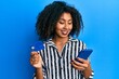 © Krakenimages.com - Beautiful african american woman with afro hair holding smartphone and credit card smiling with a happy and cool smile on face. showing teeth.
