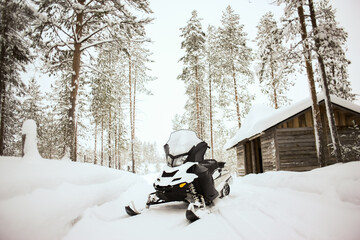 White snowmobile is standing on a snow on a background of a winter scenic landscape with trees and house.