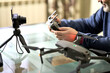 © ROMAN DZIUBALO - A man writes a blog in front of a camera about taking photos with a quadrocopter. He is holding the remote control from the drone. Selective focus.