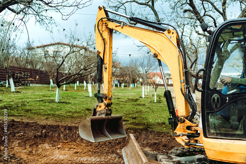 Obraz Dibond Landscaping works in the garden at construction site with mini yellow excavator