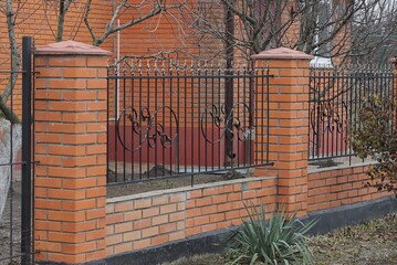 Canvas Print - part of the red fence wall of black iron bars and  bricks on the street