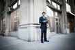 © Cavan Images - Businessman holding digital tablet and standing against building