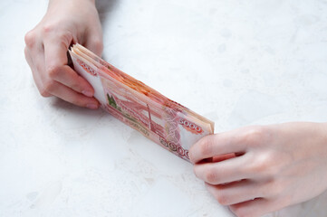 Wall Mural - Women's hands hold a stack of large bills of five thousand rubles at the table