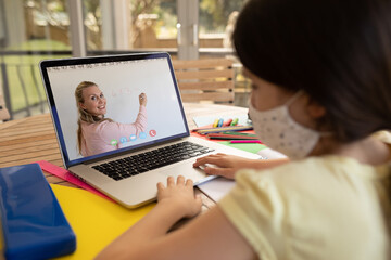 Sticker - Female student wearing face mask having a video call with female teacher on laptop at school