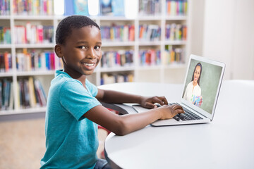 Poster - Portrait of male african american student having a video call with female teacher on laptop at libra