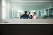 © Cavan Images - Business people discussing in office seen through window