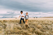 © Cavan Images - Happy brothers running while playing on grassy field against cloudy sky