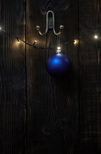 Blue Bauble Hanging By Illuminated String Lights On Wooden Wall During Christmas