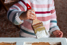 Close-up Of A Little Girl's Hand Painting An Old Furniture With A Brush, In White Color
