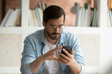 Wall Mural - serious young man in glasses look at cellphone screen read news online on gadget. concentrated cauca