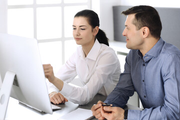 Cheerful smiling businessman and woman working with computer in modern office. Headshot at meeting or workplace. Teamwork, partnership and business concept