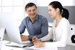 © rogerphoto - Cheerful smiling businessman and woman working with computer in modern office. Headshot at meeting or workplace. Teamwork, partnership and business concept