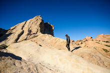 Friends Hiking On Rock Formations Against Clear Blue Sky During Sunny Day