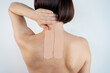 © PINKASEVICH - Kinesiology beige taping on the human back on a gray background with a copy space. Dynamic functional bandage taping on the girl's neck. Solution for back and neck pain. Headache.