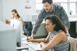 © Cavan Images - Businessman standing by female colleague using desktop computer at desk