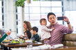 © Cavan Images - Father taking selfie with baby girl while sitting with family in restaurant