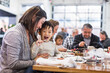 © Cavan Images - Happy mother and son sitting at table in restaurant with family in background