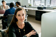 © Cavan Images - Portrait of businesswoman sitting desk while colleagues discussing in background