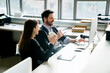 © Cavan Images - Smiling businessman using desktop computer while sitting with female colleague in office