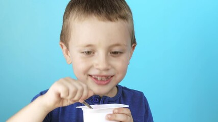 Wall Mural - Little boy eatiing yogurt on blue background