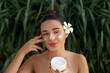 © verona_studio - Beauty Woman Concept. Skin care. Young model with Soft skin holding cosmetic cream. Portrait of female applying moisturizing cream and touch own face in tropical nature