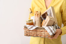 Woman Holding Gift Basket With Products On Light Background, Closeup
