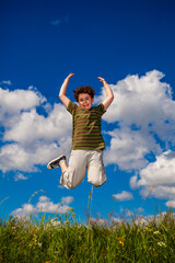 Wall Mural - Boy jumping on green meadow against blue sky
