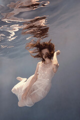 Wall Mural - A girl in a white dress posing and somersaulting under water as if flying in zero gravity