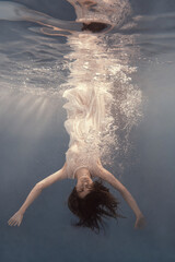 Wall Mural - A girl in a white dress posing and somersaulting under water as if flying in zero gravity